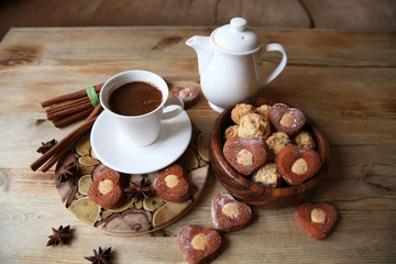 coffee in a white cup with a saucer and a white kettle with heart-shaped cookies on a rustic wooden table