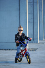 Stylishly dressed a little boy rides a bike outdoors. Happy and carefree time. Joy of childhood and fun.