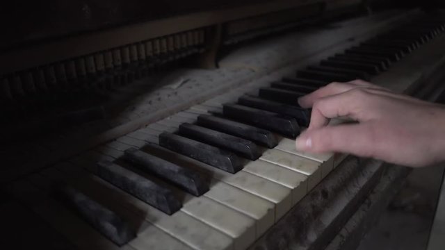 hand plays dusty old piano in dark room