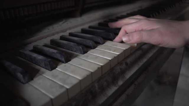 hand plays dusty old piano in dark room