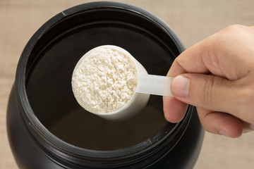 Whey Protein. Point of view of hand holding measuring scoop. Vanilla flavour. Wooden background.