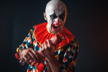 Bloody clown holds human hand, finger in his teeth