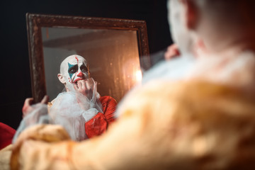 Frightened bloody clown looking at the mirror
