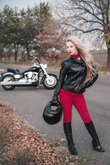 A stylish biker woman posing outdoor with motorcycle. 
