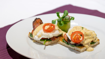 Beautiful benedict eggs with bacon, mustard sauce, and salad on a French toast