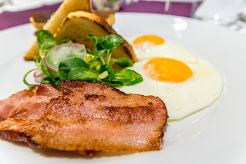 Bacon on an American breakfast plate with sunny side up eggs and french toast, close up and selective focus photo