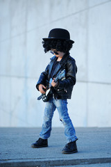 A  little, cute boy guitarist in leather jacket and sunglasses  playing guitar.  Young idol....
