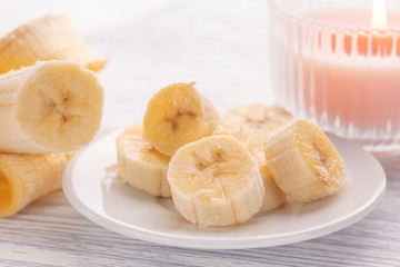 Sliced banana on a white plate and a light wooden table. Pink burning candle nearby.