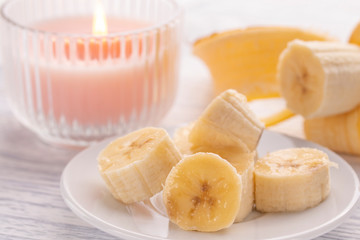 Sliced banana on a white plate and a light wooden table. Pink burning candle nearby.