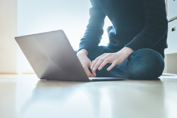 Naklejka premium Young man with a modern laptop is sitting on the wooden floor