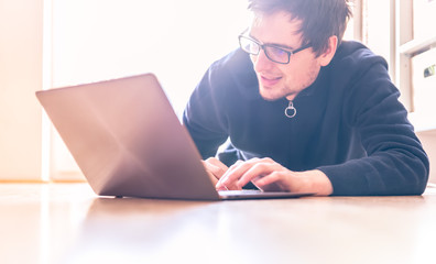Happy young man with a modern laptop is sitting on the wooden floor
