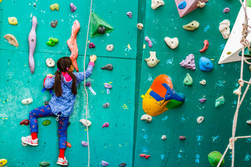 A young girl climbing a tall, indoor, man-made rock climbing wall - obrazy, fototapety, plakaty