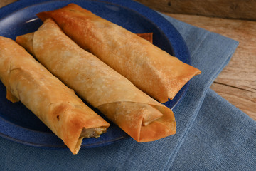 stuffed filo or yufka dough rolls with a spicy meat filling on a blue plate on a rustic wood, selected focus