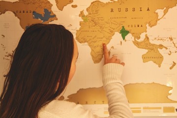 Young teenage girl pointing at a destination on a scratch map of the world on the wall