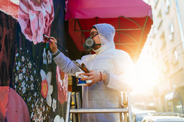 Young graffiti artist painting mural outdoors on street wall.