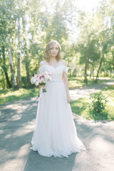 The bride in a white dress in nature in the Park. Photo shoot with a bouquet in the style of fine art.
