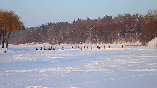 Anonymous men playing in distance hockey game outdoors using ice rink made on frozen river. Healthy lifestyle. Real time full hd video footage.