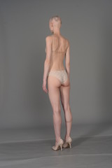 bald girl in beige lingerie posing on grey background