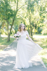 The bride in a white dress in nature in the Park. Photo shoot with a bouquet in the style of fine art.