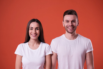 Beautiful young couple in white blank t-shirts are posing on orange background. Relationship, family, advertising