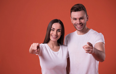 Beautiful young couple in white blank t-shirts are posing on orange background. Relationship, family, advertising