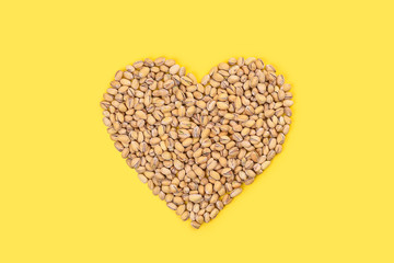 Heart of pistachios on a bright yellow background.