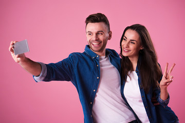 Beautiful romantic couple isolated on pink background. Attractive young woman and handsome man are making selfie, smiling and have a fun