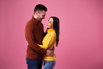 Young cheerful loving couple dressed in sweaters hugging isolated over pink background