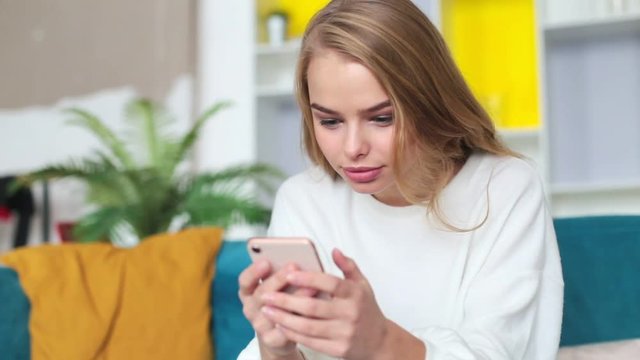 happy young woman sitting on sofa playing with her cell phone and winning