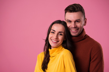 Fototapeta premium Young cheerful loving couple dressed in sweaters hugging isolated over pink background