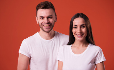 Beautiful young couple in white blank t-shirts are posing on orange background. Relationship, family, advertising