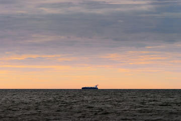 Fototapeta premium Cargo ship silhouette on the horizon. Container vessel sailing through the Baltic Sea at sunset. Gdansk Bay, Pomerania, Poland.