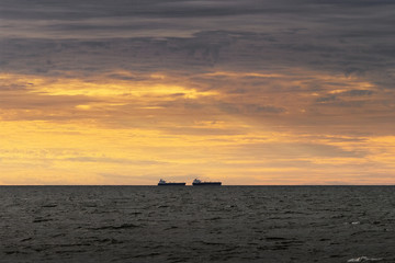 Fototapeta premium Cargo ships silhouettes on the horizon. Two cargo vessels sailing through the Baltic Sea at sunset. Gdansk Bay, Pomerania, Poland.
