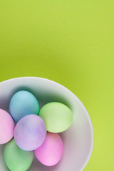 Overhead view of brightly painted easter eggs in a white bowl on green background