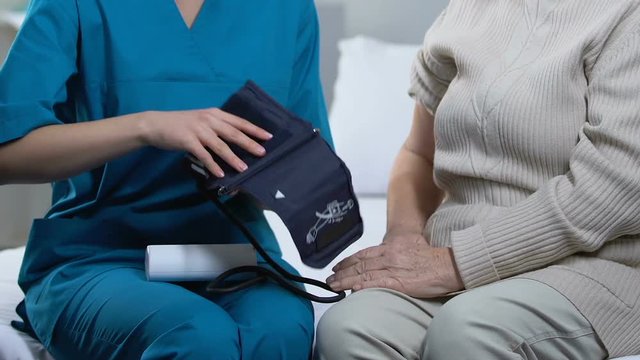 Nurse measuring aged female patient blood pressure in nursing home, medicare - Powered by Adobe