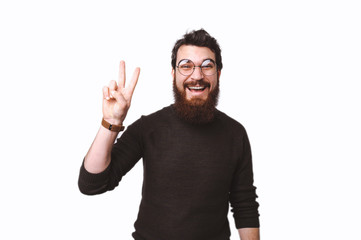 Fototapeta premium Peace, attractive bearded man in glasses showing victory sign and smiling at the camera