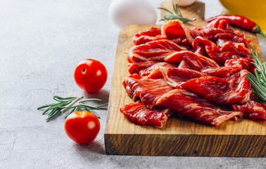 Raw sliced beef bacon ready for cooking on light concrete background.