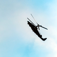 Silhouette of combat helicopter doing aerobatic maneuvers against the blue sky and clouds