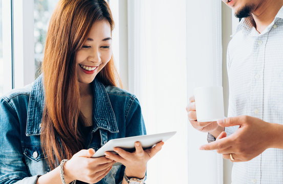 Young asian casual business team happy smiling and relax while standing meeting about marketing on digital tablet in modern coworking space office