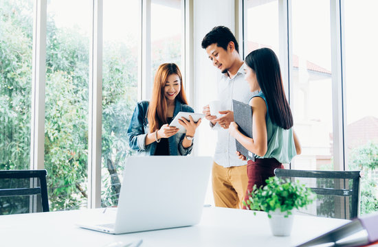 Young asian casual business team happy smiling while standing relax meeting about marketing on digital tablet in modern coworking space office