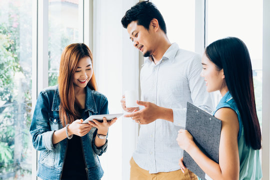 Young asian casual business team happy smiling and relax while standing meeting about marketing on digital tablet in modern coworking space office