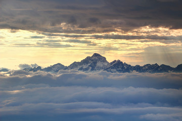Jagged snowy Triglav peak of Julijske Alpe range towering dramatically over sea of low clouds with sky in glowing orange light behind, Triglav National Park Gorenjska Kranjska Carniola Slovenia Europe