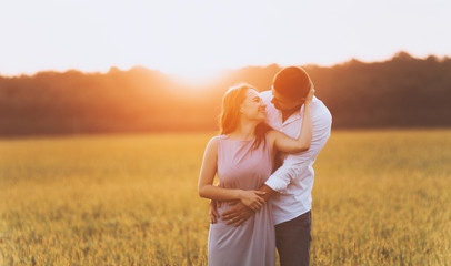 A couple photo , man hugging woman from behind and looking to each other, in nature on sunset