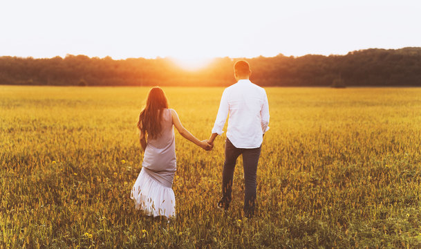 A back view photo of handsomesouple in meadow on the sunset or sunrise