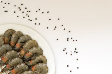 Fresh uncooked king prawns in a white plate and black pepper peas on a white background. Delicacy, tasty and healthy sea food, close up, top view