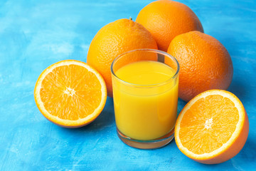 Orange fresh drink, glass of juice and ripe citrus fruits on a blue background