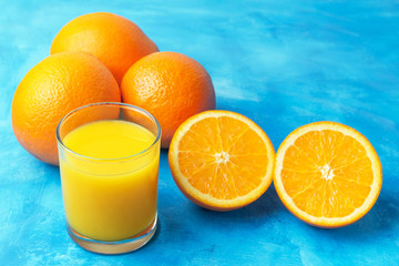 Orange fresh drink, glass of juice and ripe citrus fruits on a blue background