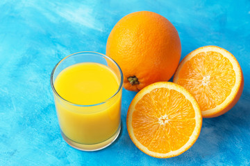 Orange fresh drink, glass of juice and ripe citrus fruits on a blue background
