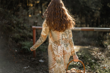 Young woman with long red hair in a linen dress gathering mushrooms in the forest in the bast basket