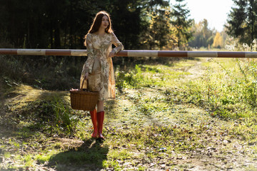 Young woman with long red hair in a linen dress gathering mushrooms in the forest in the bast basket